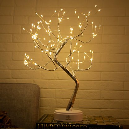 Decorative LED tree with lights on a stand against a brick wall.