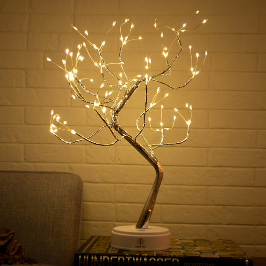 Decorative LED tree with lights on a stand against a brick wall.