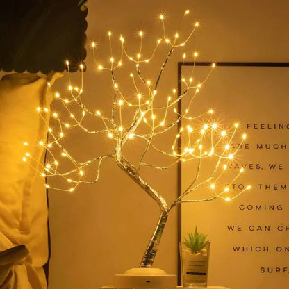Decorative LED tree with warm lights on a table against a wall with text.
